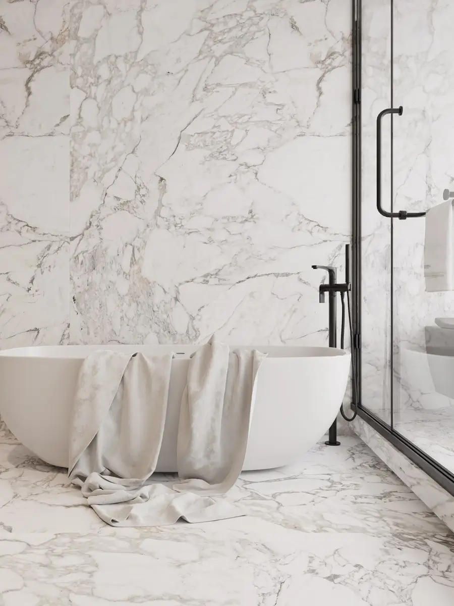 Oval freestanding bath against a marble wall with matte black floor-mounted tapware